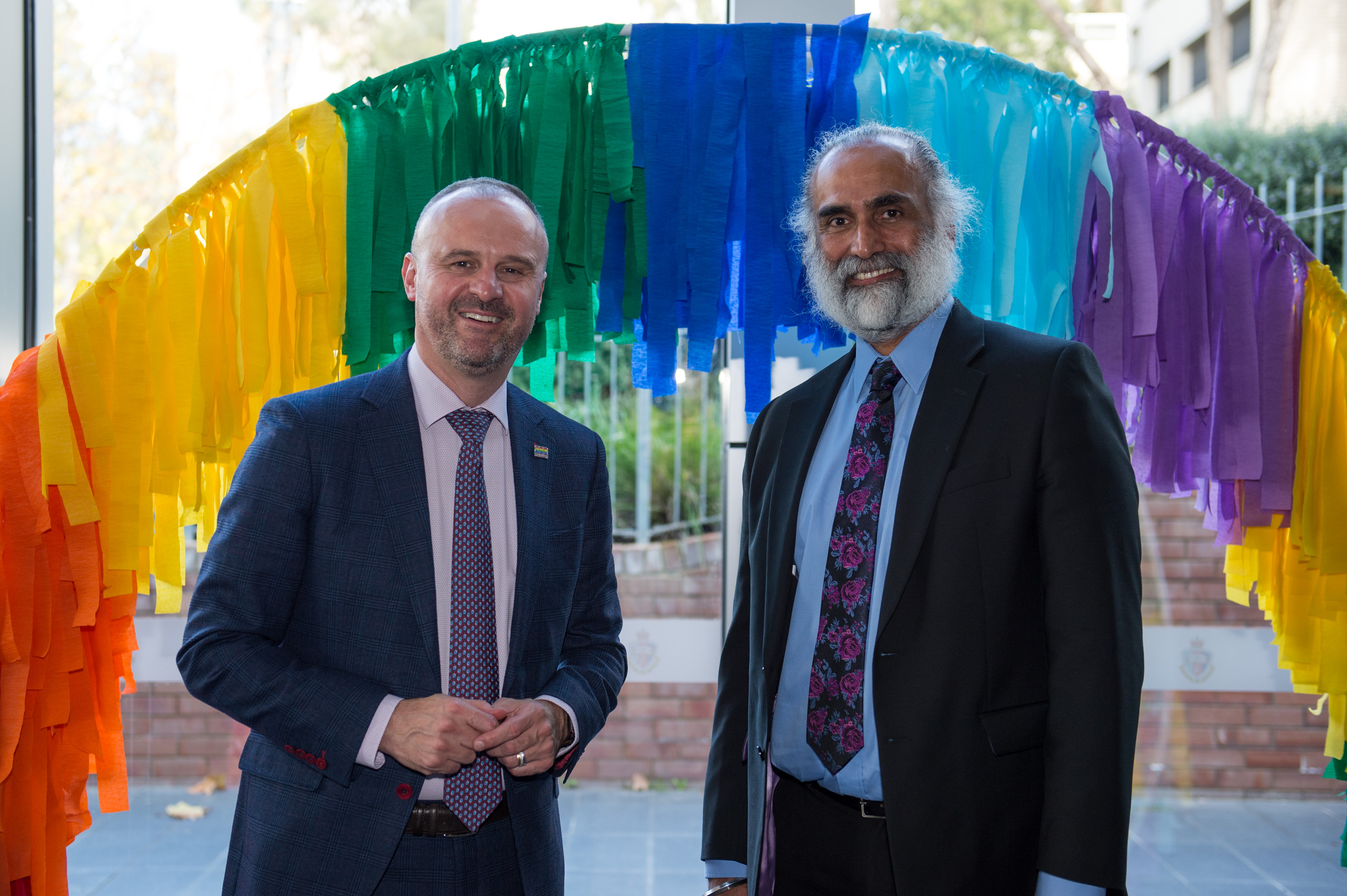 Andrew Barr and Harvi Sidhu stand under a rainbow banner in celebration of IDAHOBIT 