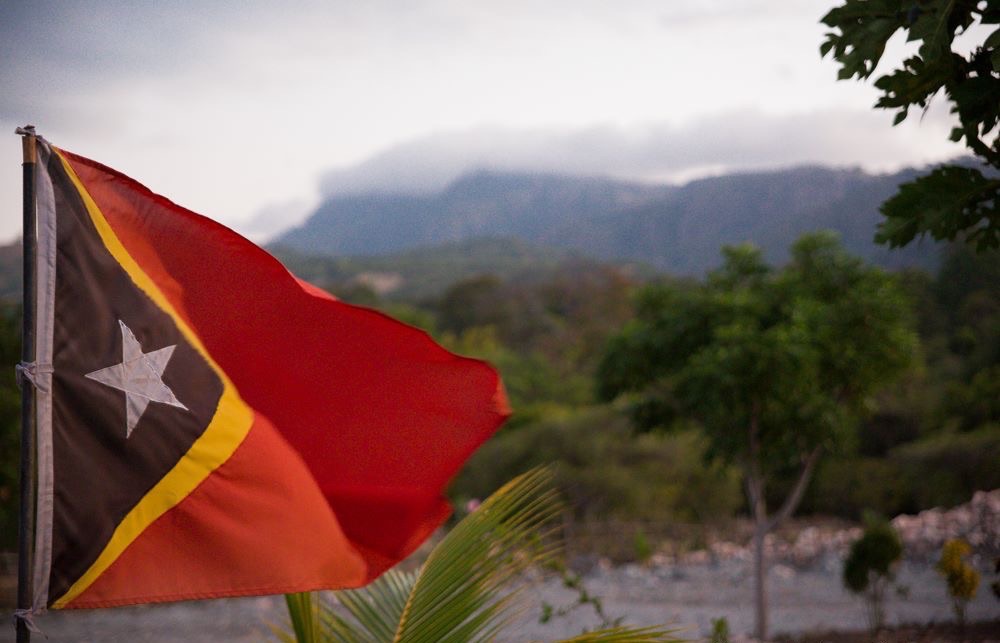East Timor flag flies with the country&#039;s landscape in the background. 