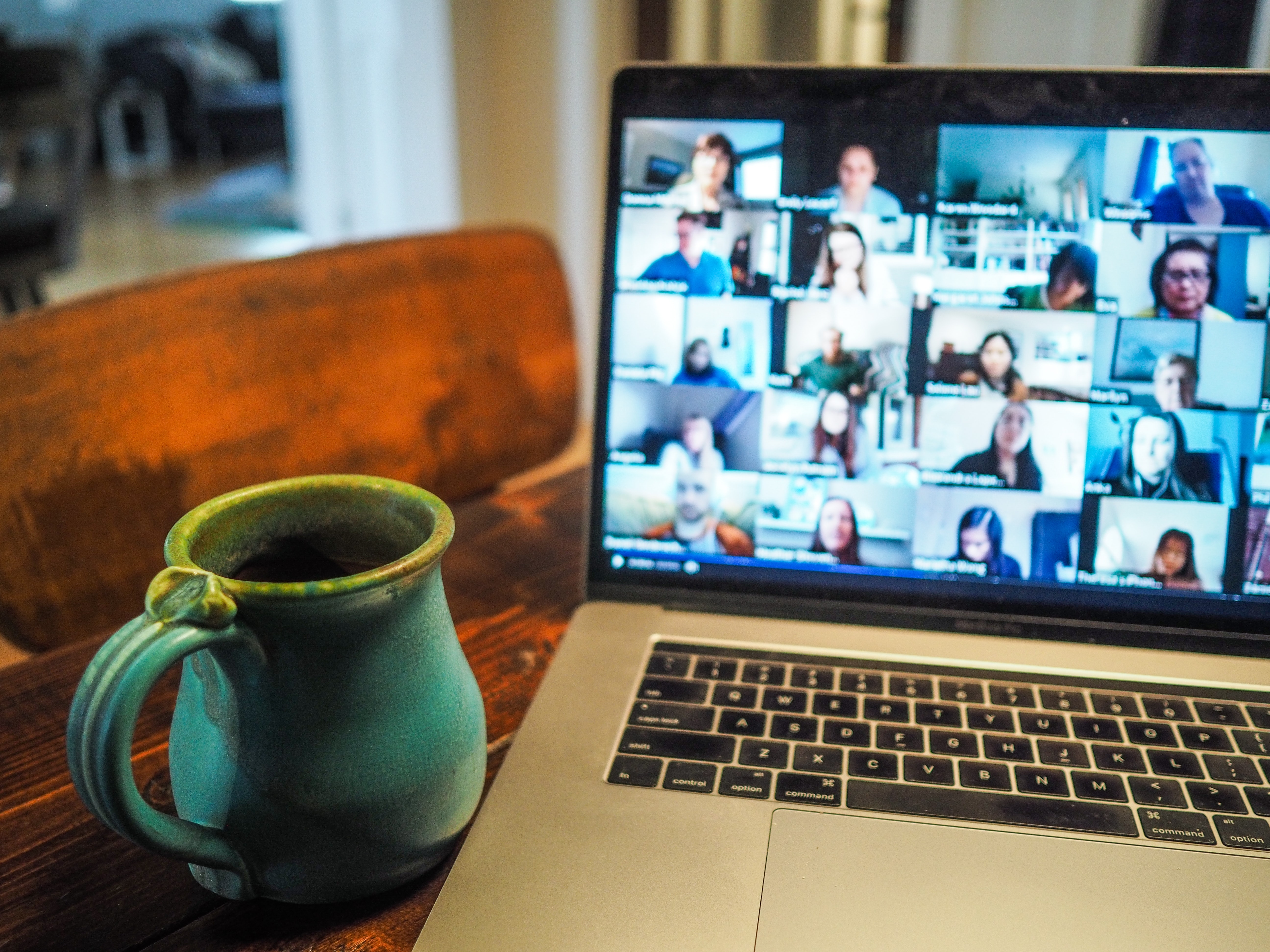 A laptop screen filled with a large Zoom chat and a coffee mug nearby. 