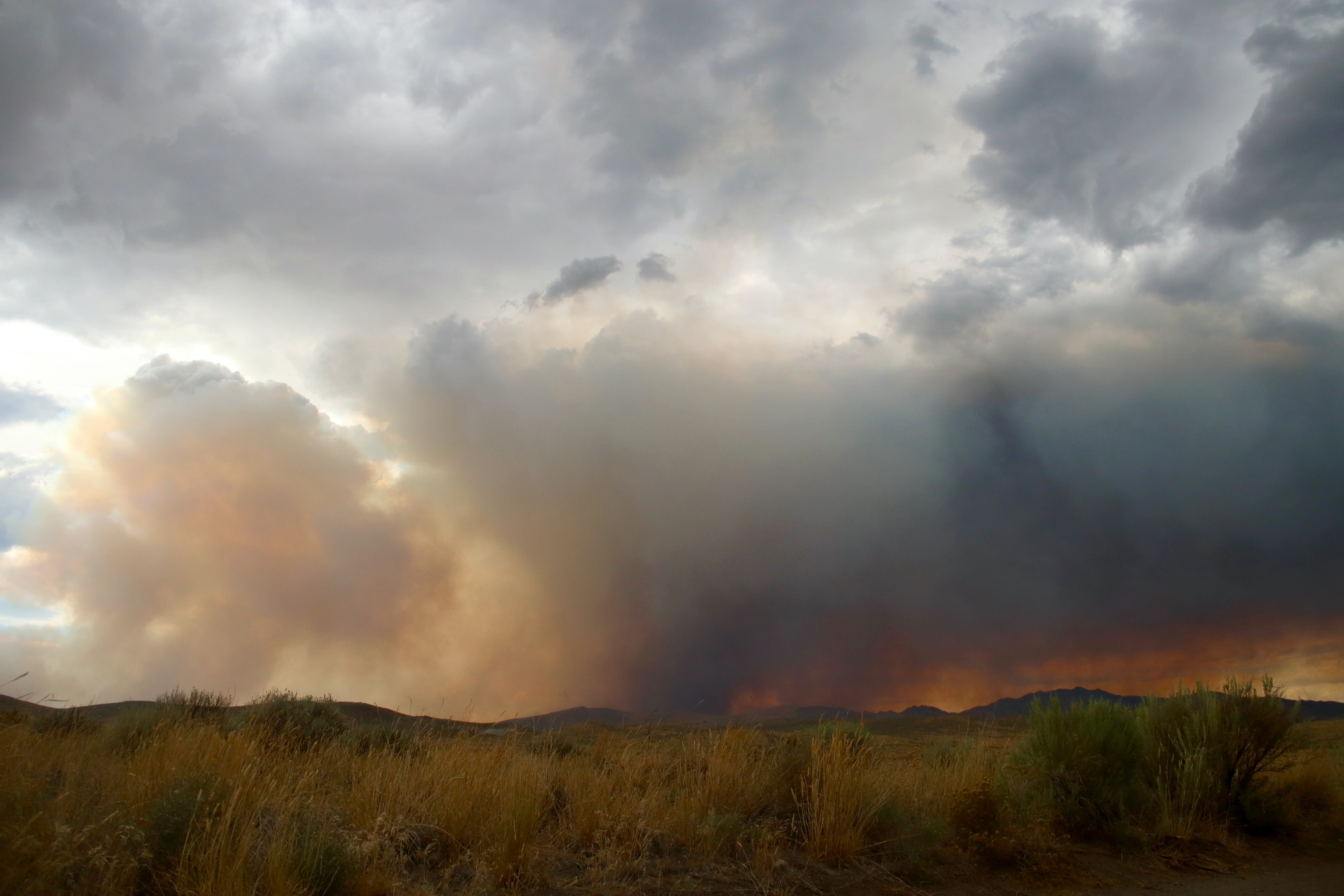 Smoke fills the air and fire burns on the horizon of a hilly landscape. 