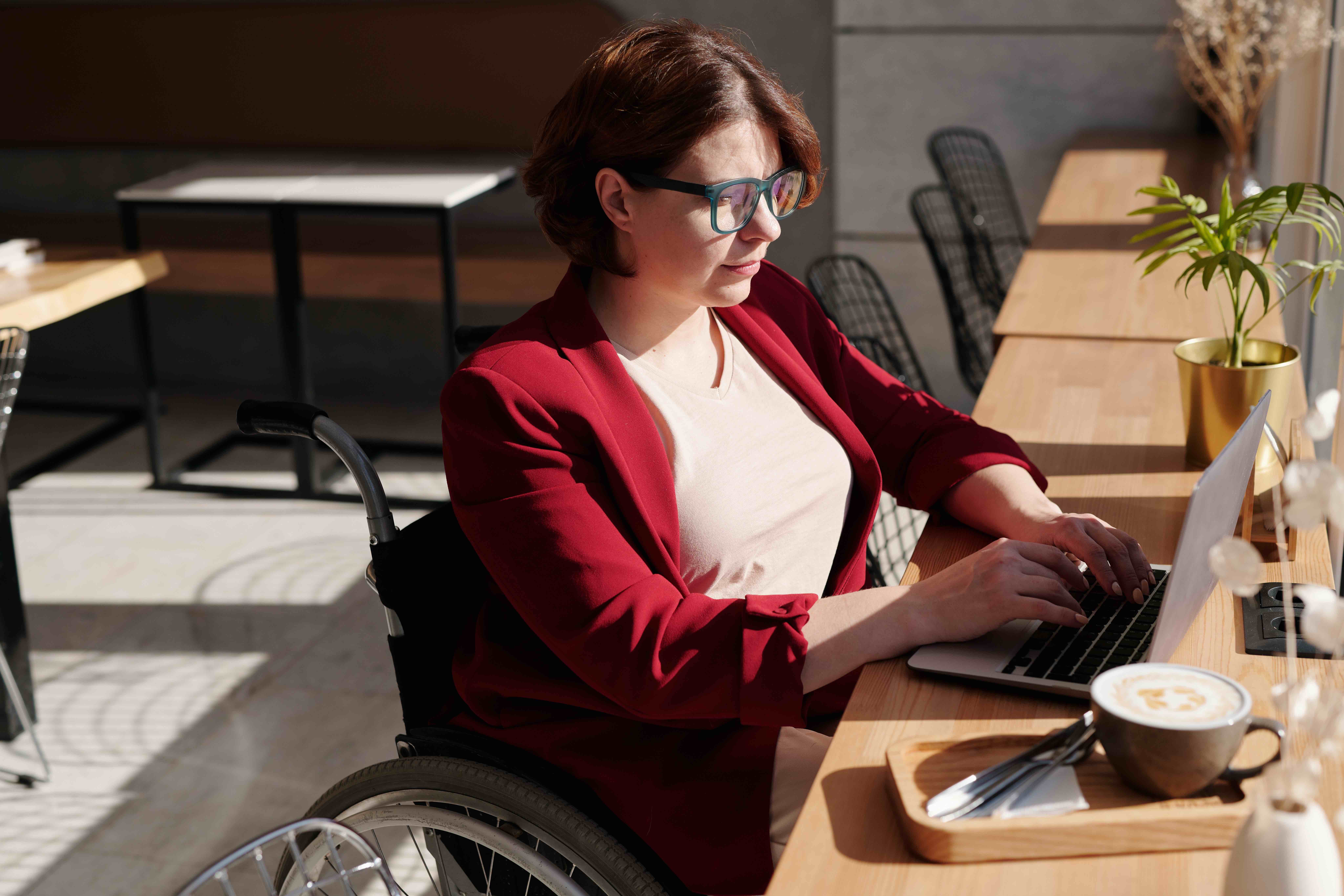 A woman sits in a wheelchair with laptop and coffee
