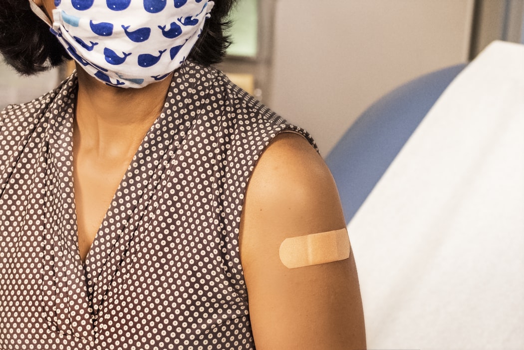 Woman wearing a mask with a Band-Aid on her left arm.