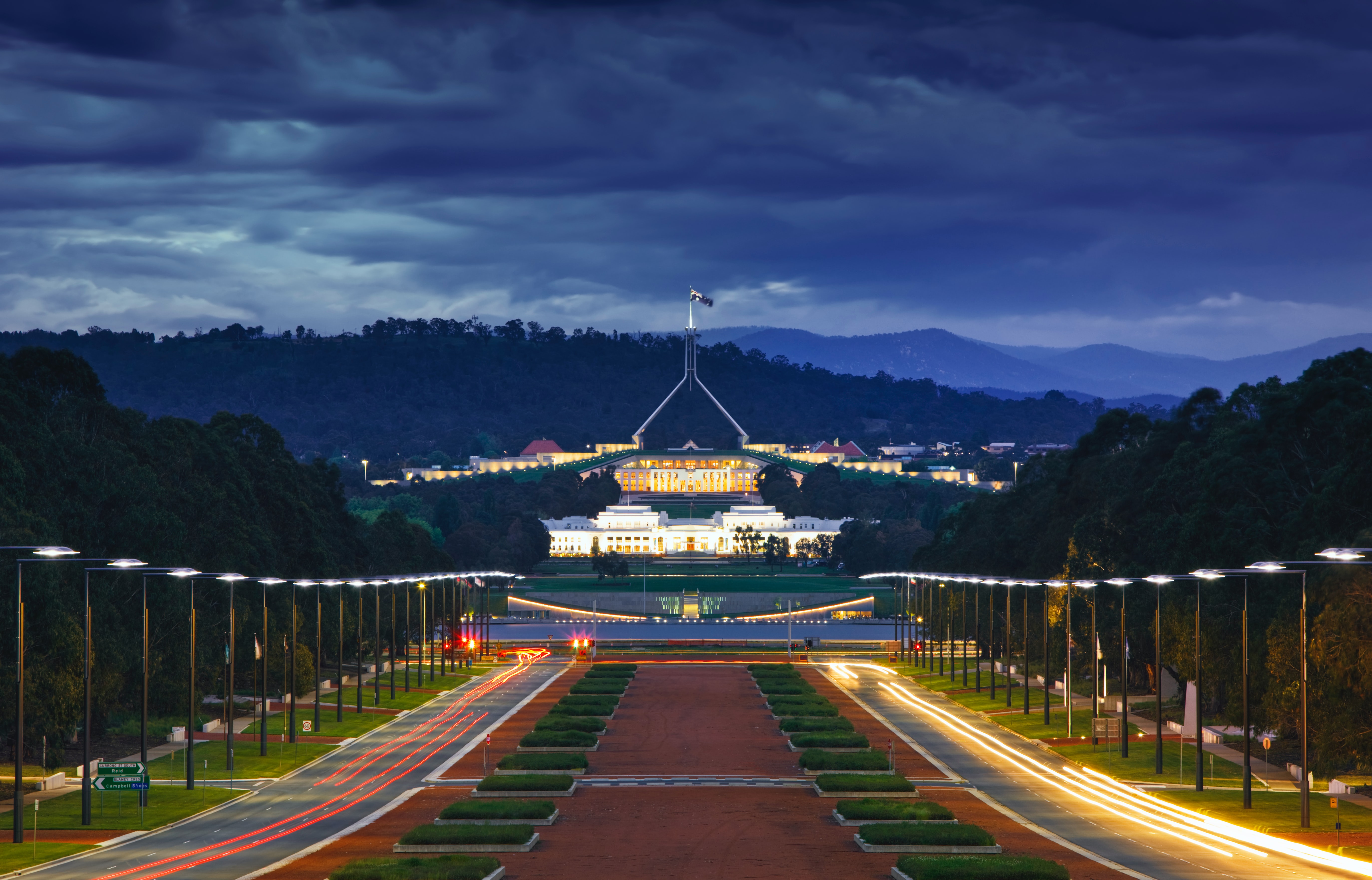 Parliament House (Australia) at dusk, shot from the perspective of the War Memorial. Lights line the avenue leading to Parliament House in the near distance.