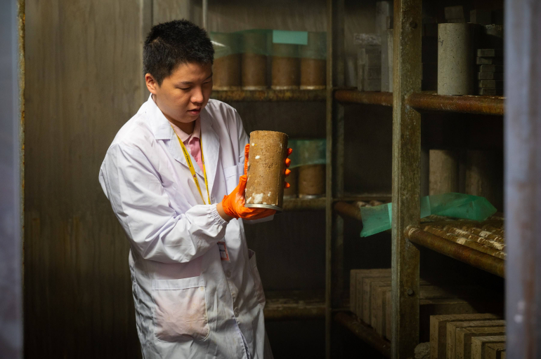 Student in lab coat holds cylinder of packed soil
