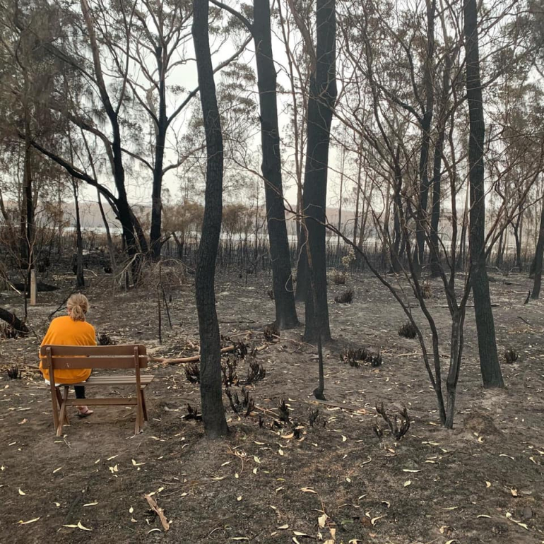 Image of woman seated in bush that has been burnt by fires