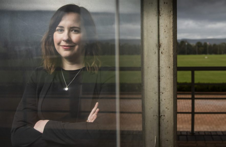 Dr Megan Evans' reflection in a window, with a grassy field behind her. She is smiling and has her arms confidently crossed.