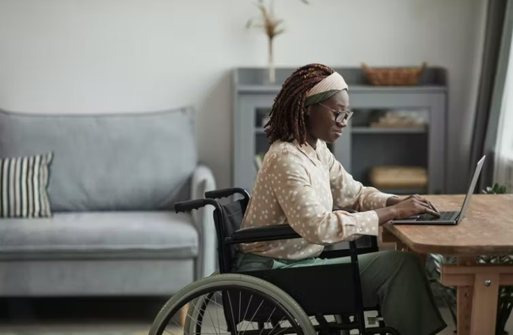 A woman sits in a wheelchair and types on a laptop.