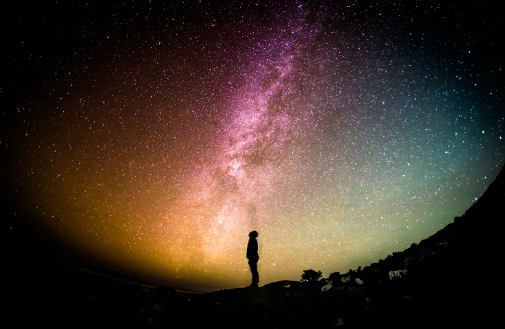 The silhouette of a person stands in the foreground of a colourful night sky